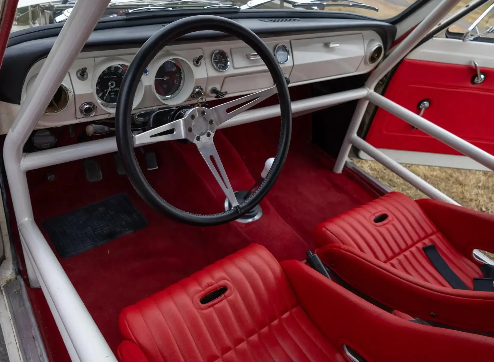 1966 Ford Cortina race car interior showing SCCA roll cage with door bars and red bucket seats with Willans harnesses