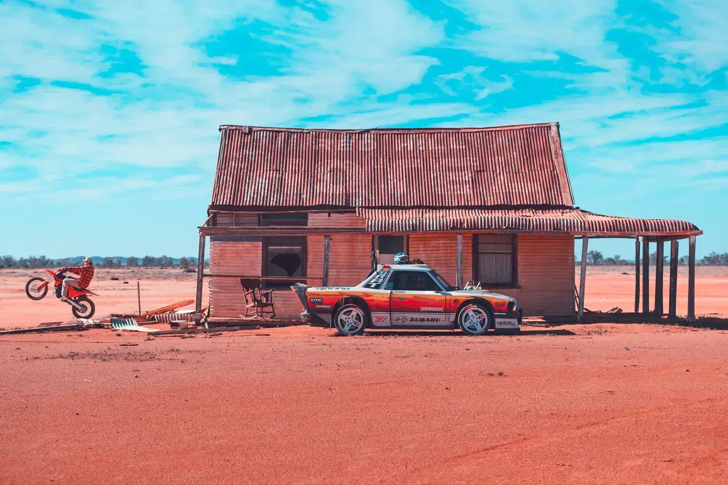 Subaru Brataroo rally car jumping through red desert sand dunes in Australian outback with dust trail