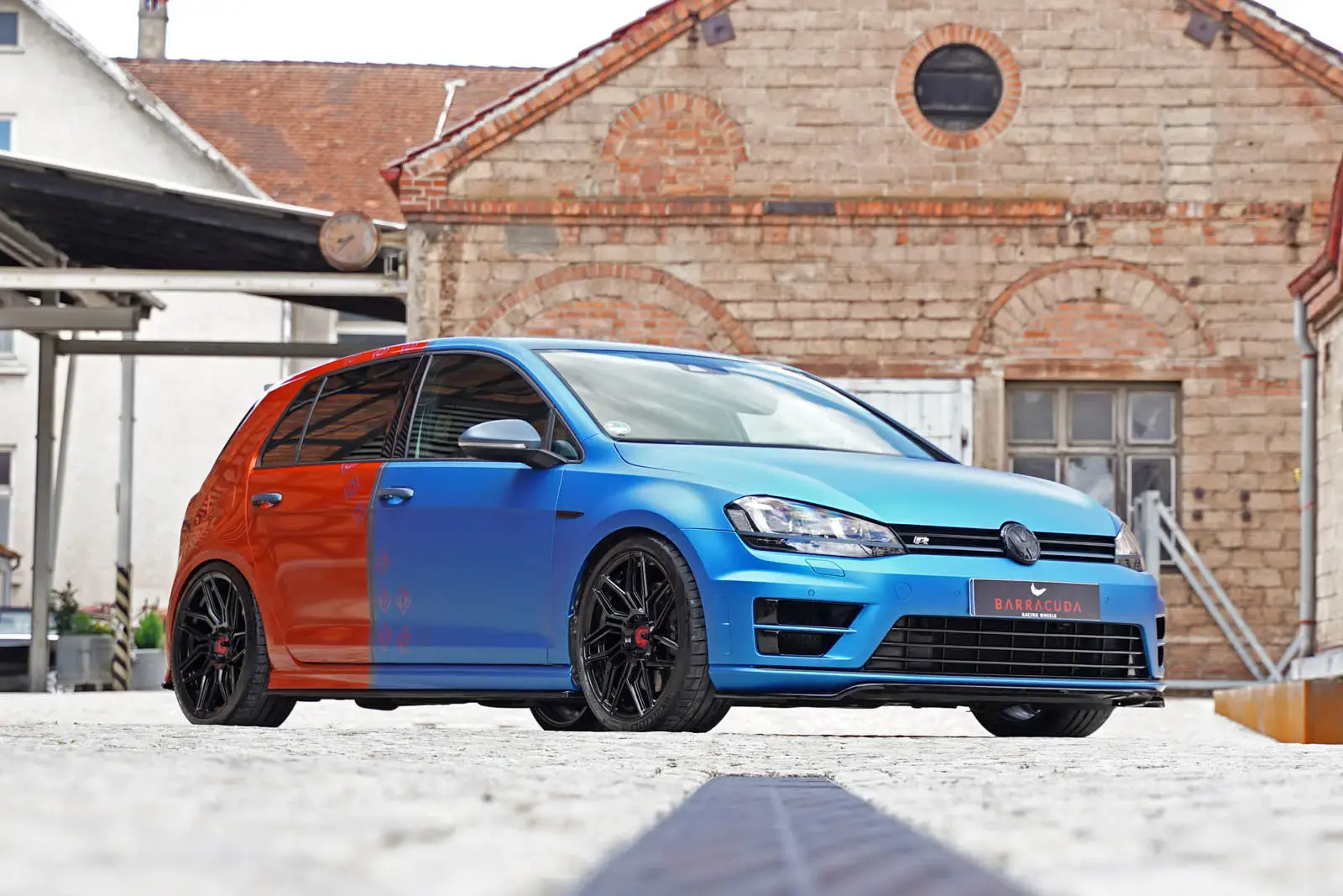 Front three-quarter view of modified Volkswagen Golf R Mk7 showing blue wrap section, Rieger front lip, and Barracuda wheels